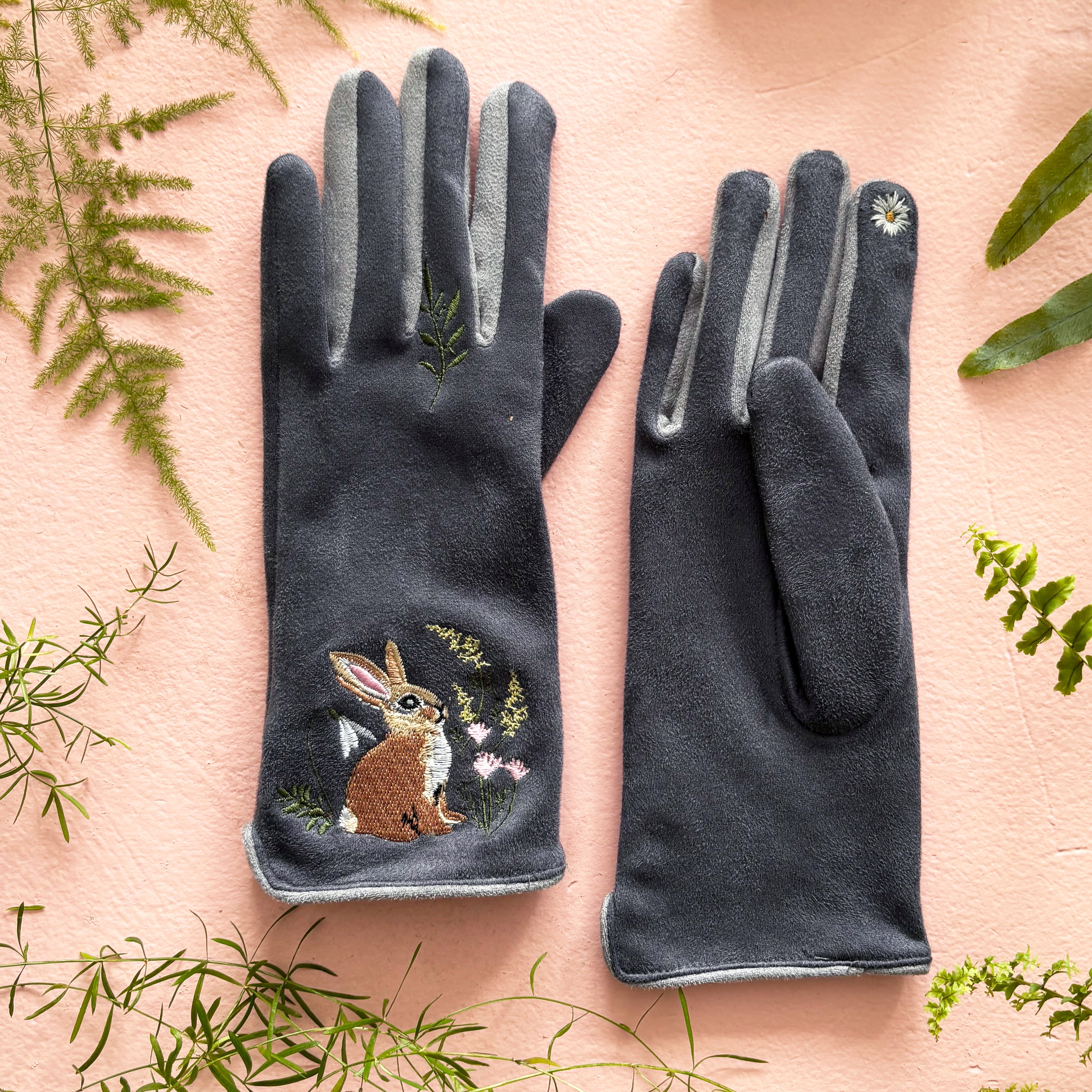 Both rabbit gloves flat on pink background with greenery showing embroidery