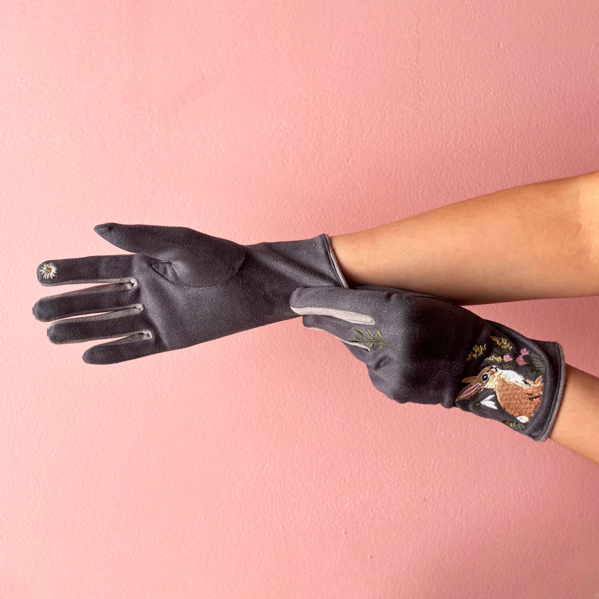 Rabbit gloves worn on hands showing embroidered detail on pink background