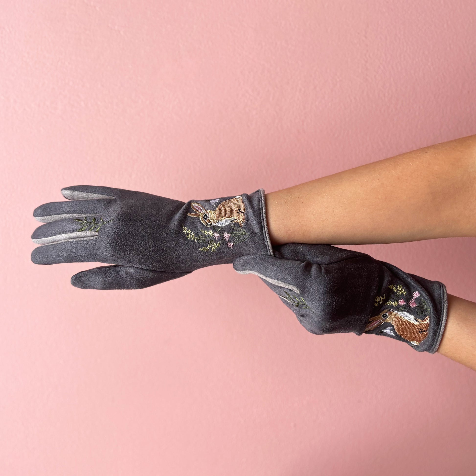 Embroidered rabbit gloves worn on hands front view against pink background