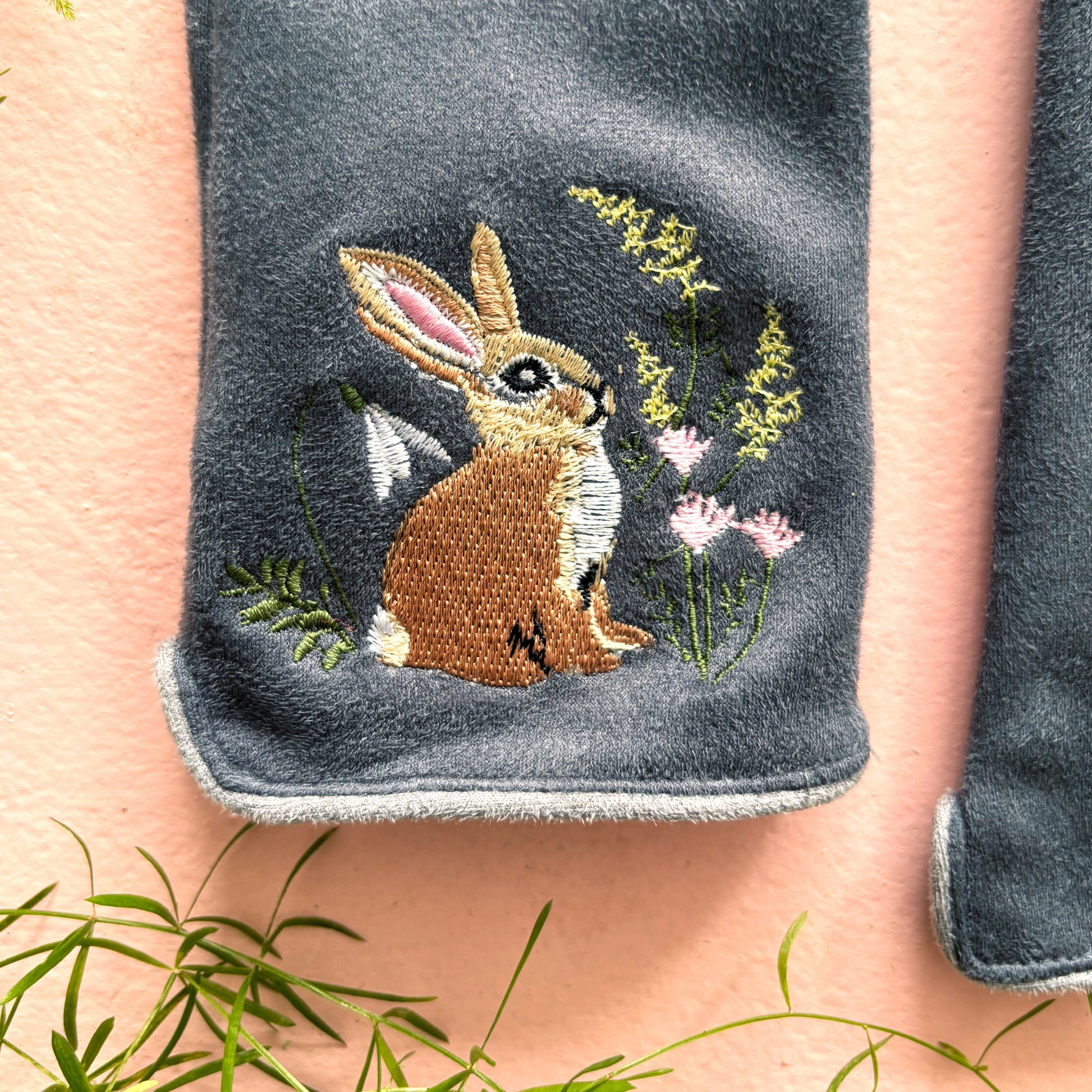 Close-up of embroidered rabbit among wildflowers on grey suedette glove