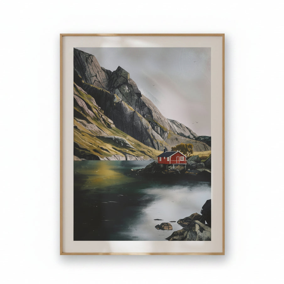 A framed landscape art print depicting a red cabin on a rocky shore next to a calm lake, surrounded by steep mountains and a misty sky, in a light wood frame with a white mat.
