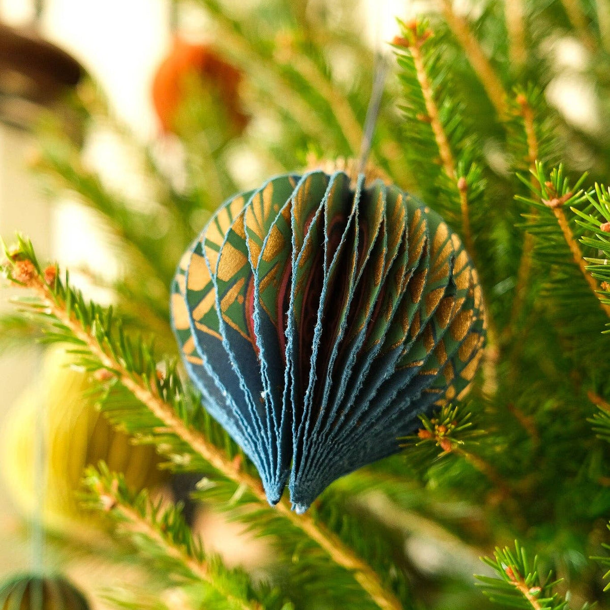 Blue Bauble Honeycomb Christmas decoration with gold pattern hanging on a real fir tree