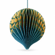A close-up of a blue and gold accordion-style paper Christmas ornament hanging among green pine tree branches.
