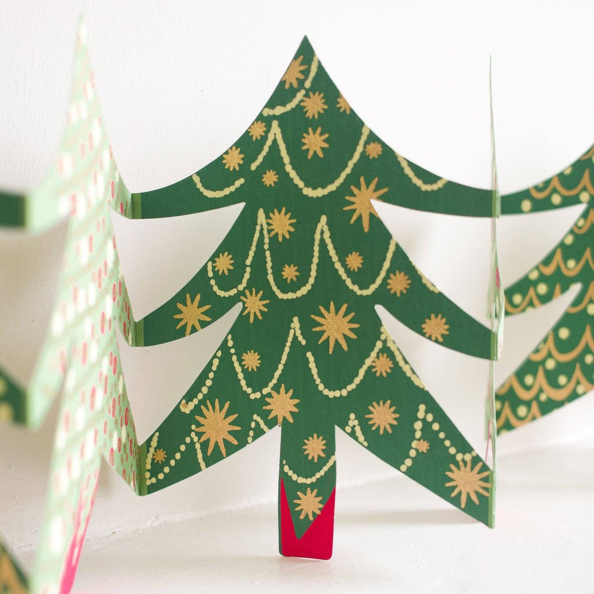 Christmas Trees Concertina Garland, green trees with gold stars, standing open on a white shelf