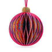 A close-up of a decorative hanging ornament shaped like a striped ball, suspended in front of a blurred green tree with colorful paper garlands nearby.
