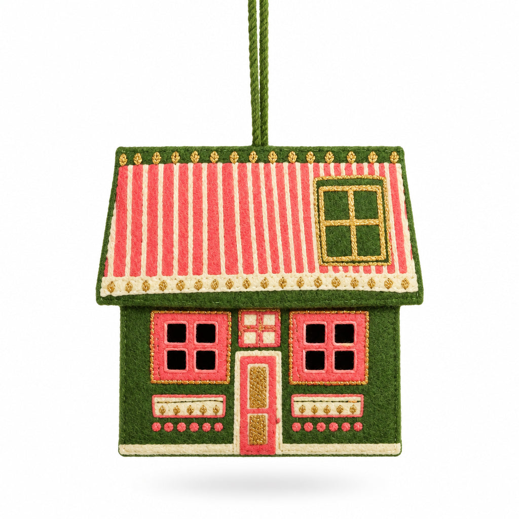 A handcrafted gingerbread house Christmas ornament hanging from a green Christmas tree branch, with other ornaments blurred in the background.