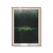 Framed artwork of a landscape with a house in the middle of a forest on a beige wall.