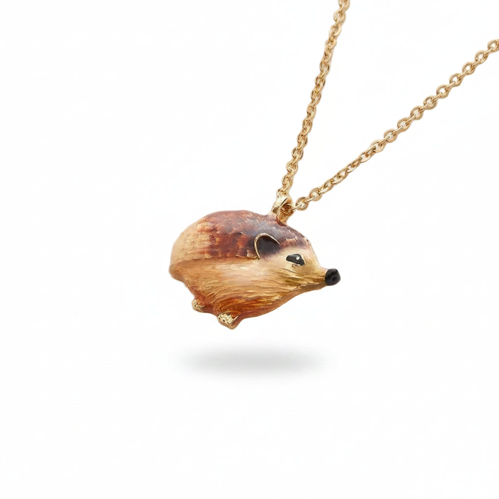 Enamel hedgehog pendant hanging on gold-plated chain against cream background
