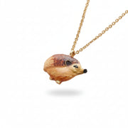 Enamel hedgehog pendant hanging on gold-plated chain against cream background