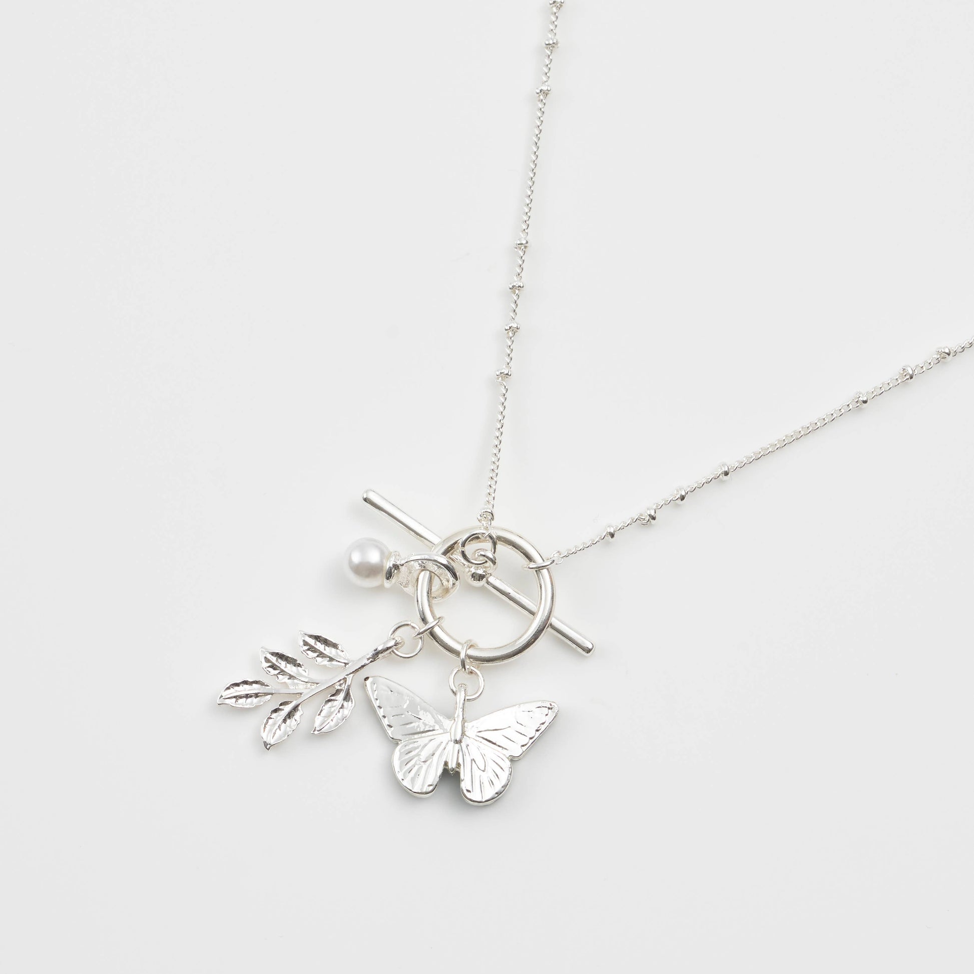 Close-up of silver butterfly charm cluster with leaf and pearl