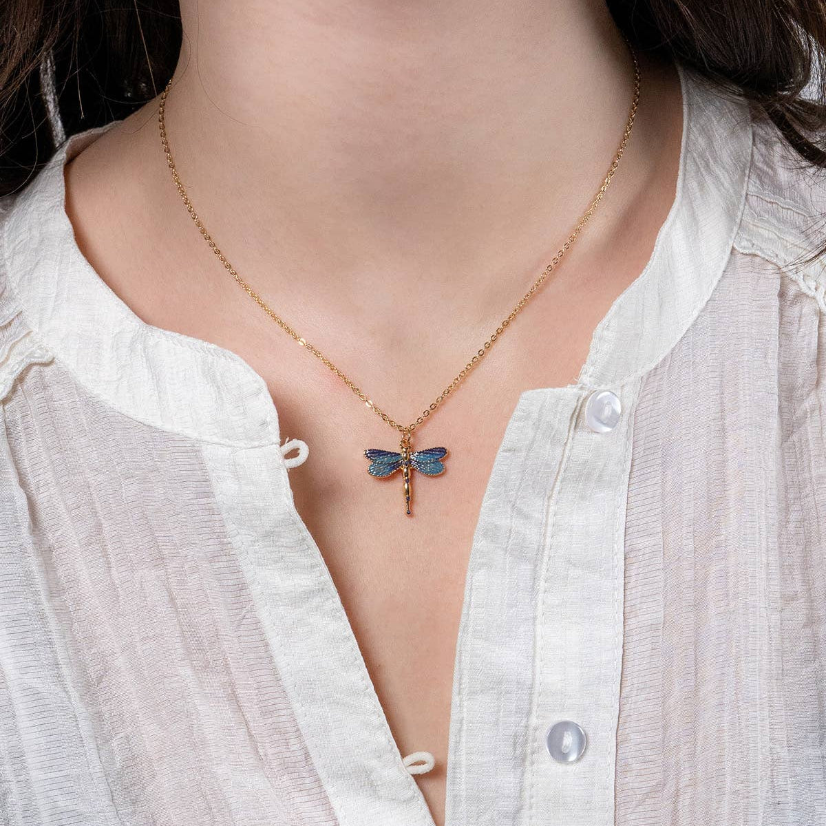 Dragonfly pendant necklace worn by model in white blouse at her neckline