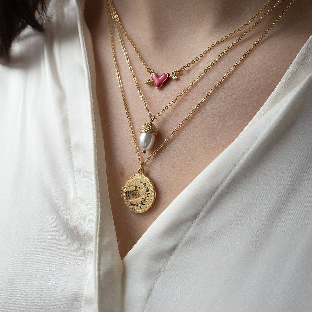 Running bunny locket worn layered with gold necklaces on white blouse