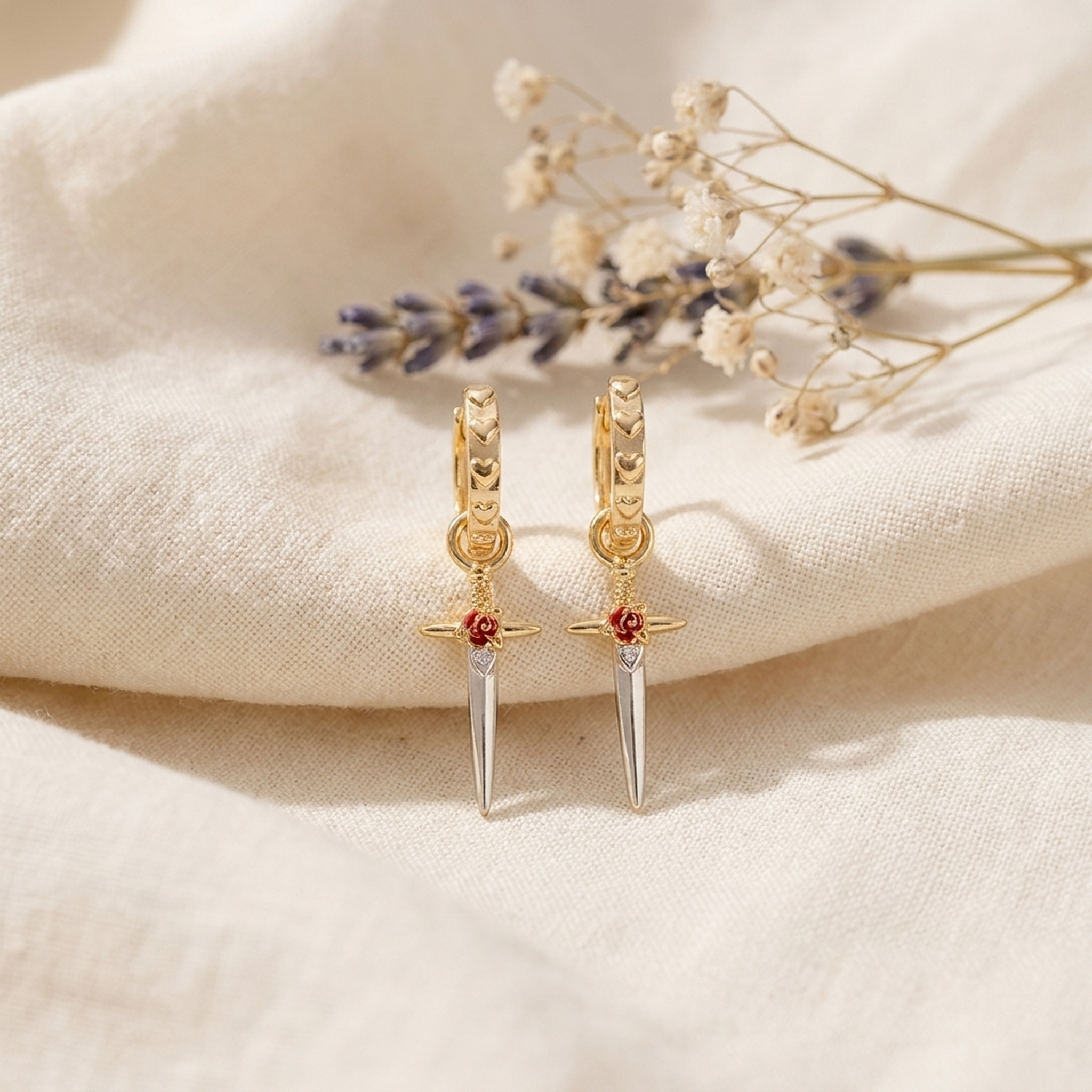 Rose Dagger Huggie Earrings styled on cream linen with dried flowers