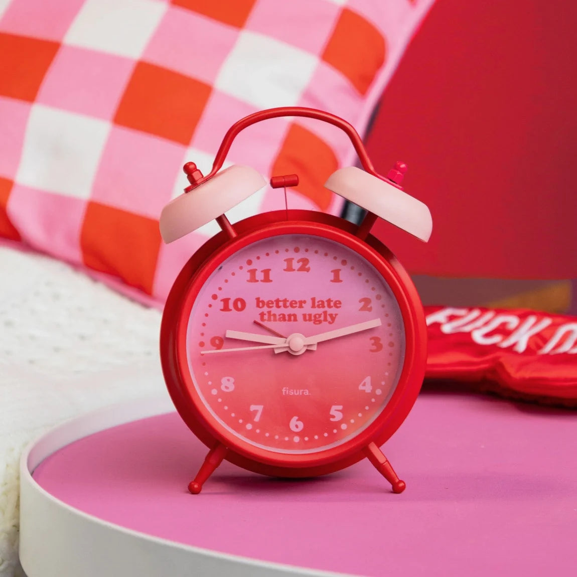 Red alarm clock on a pink table against a pink gingham backdrop