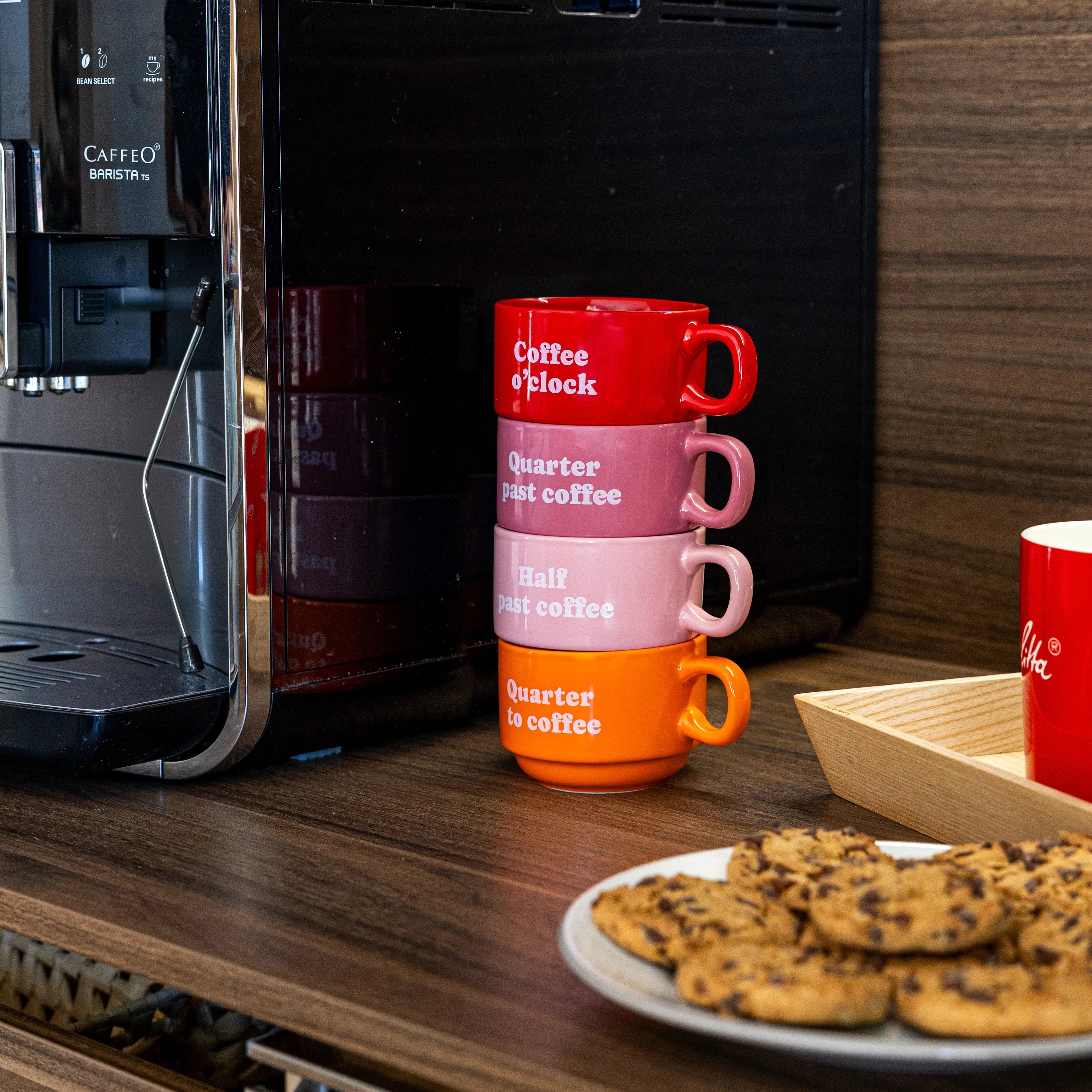 Stacked Coffee Clock mugs on a kitchen counter beside a plate of pastries