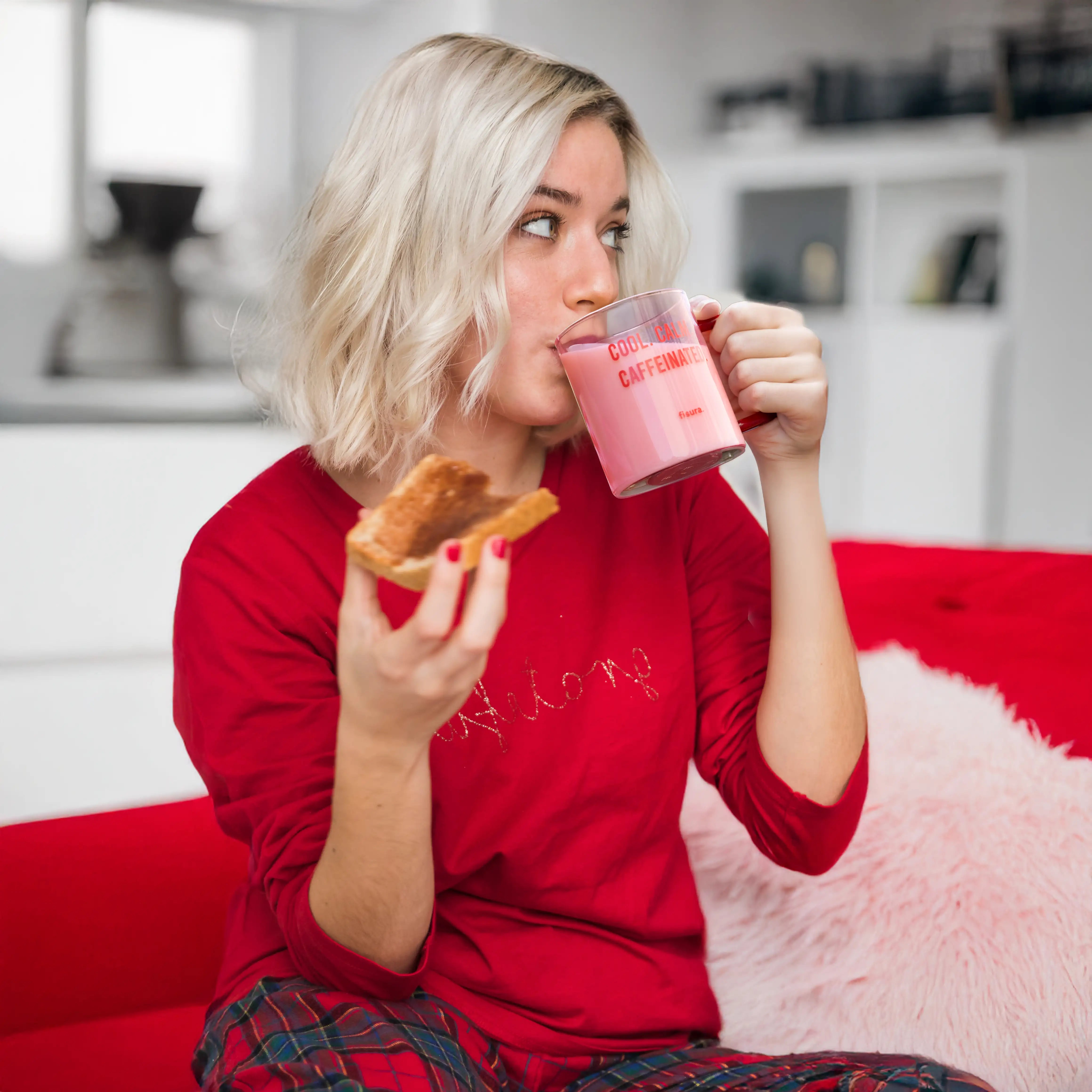Person in red drinking from the pink glass mug while holding a doughnut
