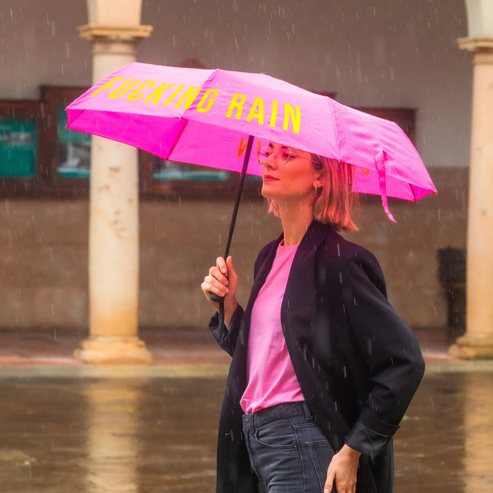 Woman walking in the rain holding the pink folding umbrella