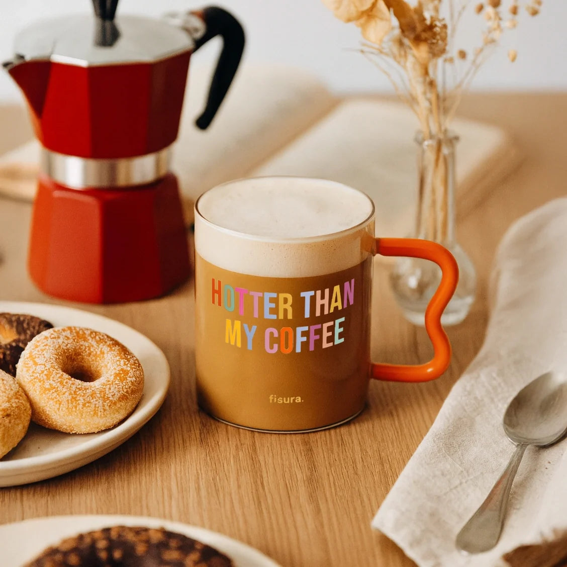 Glass mug of coffee on a table with doughnuts and a moka pot