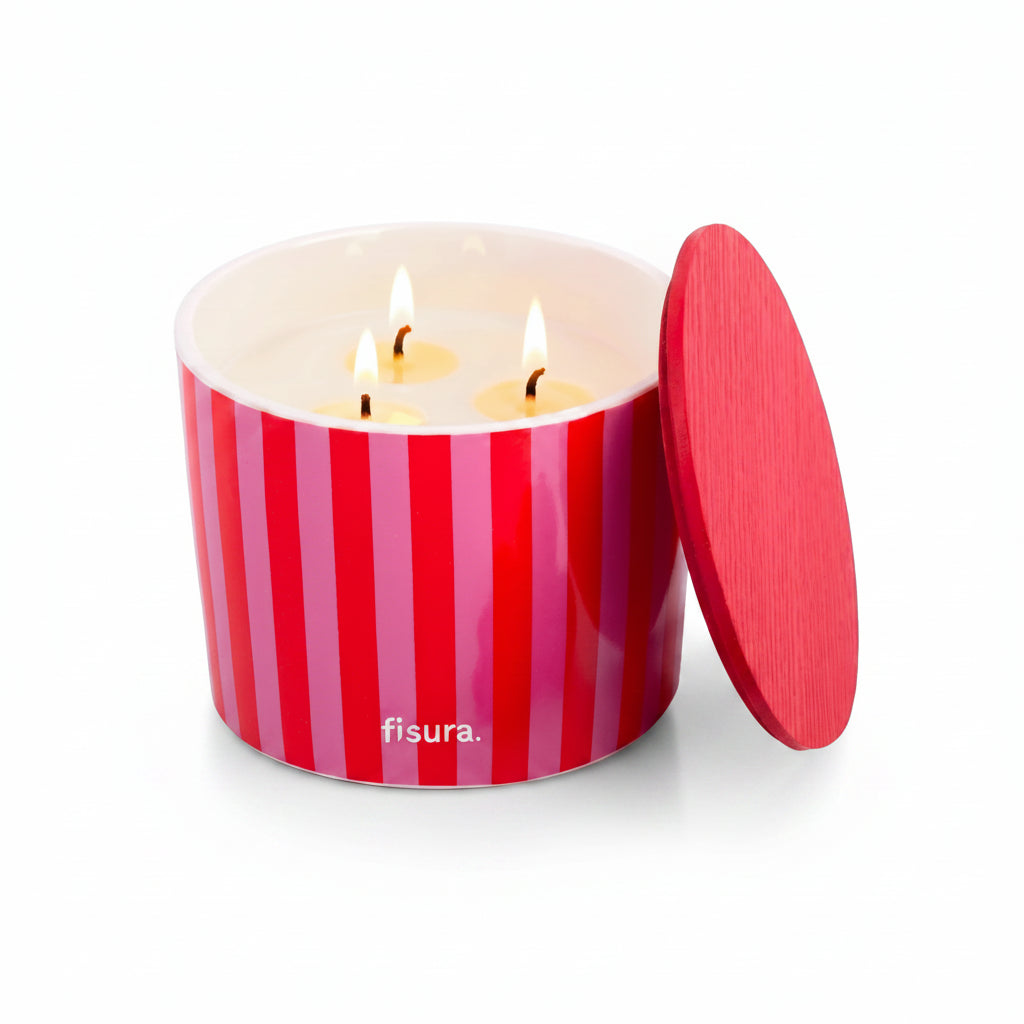 Red and pink striped ceramic candle lit, with fresh raspberries beside it