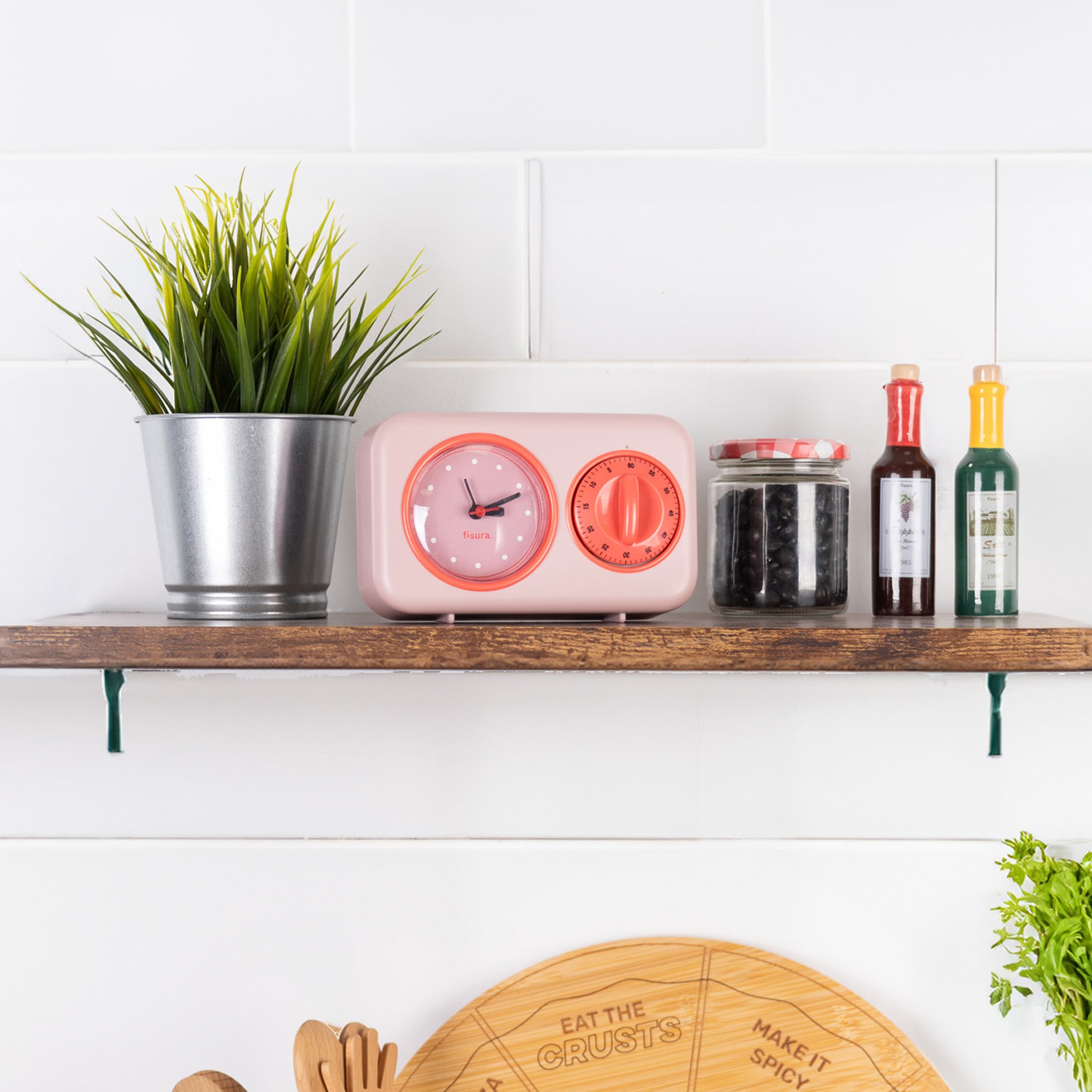 Pink kitchen timer on a wooden shelf beside jars and a small plant