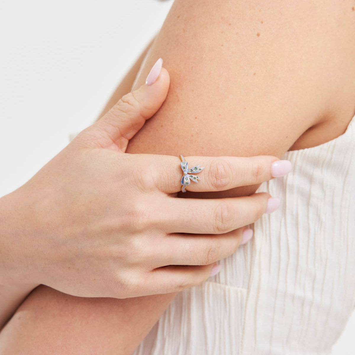 Gold and blue Forget-Me-Not bow ring worn on finger in lifestyle photo.