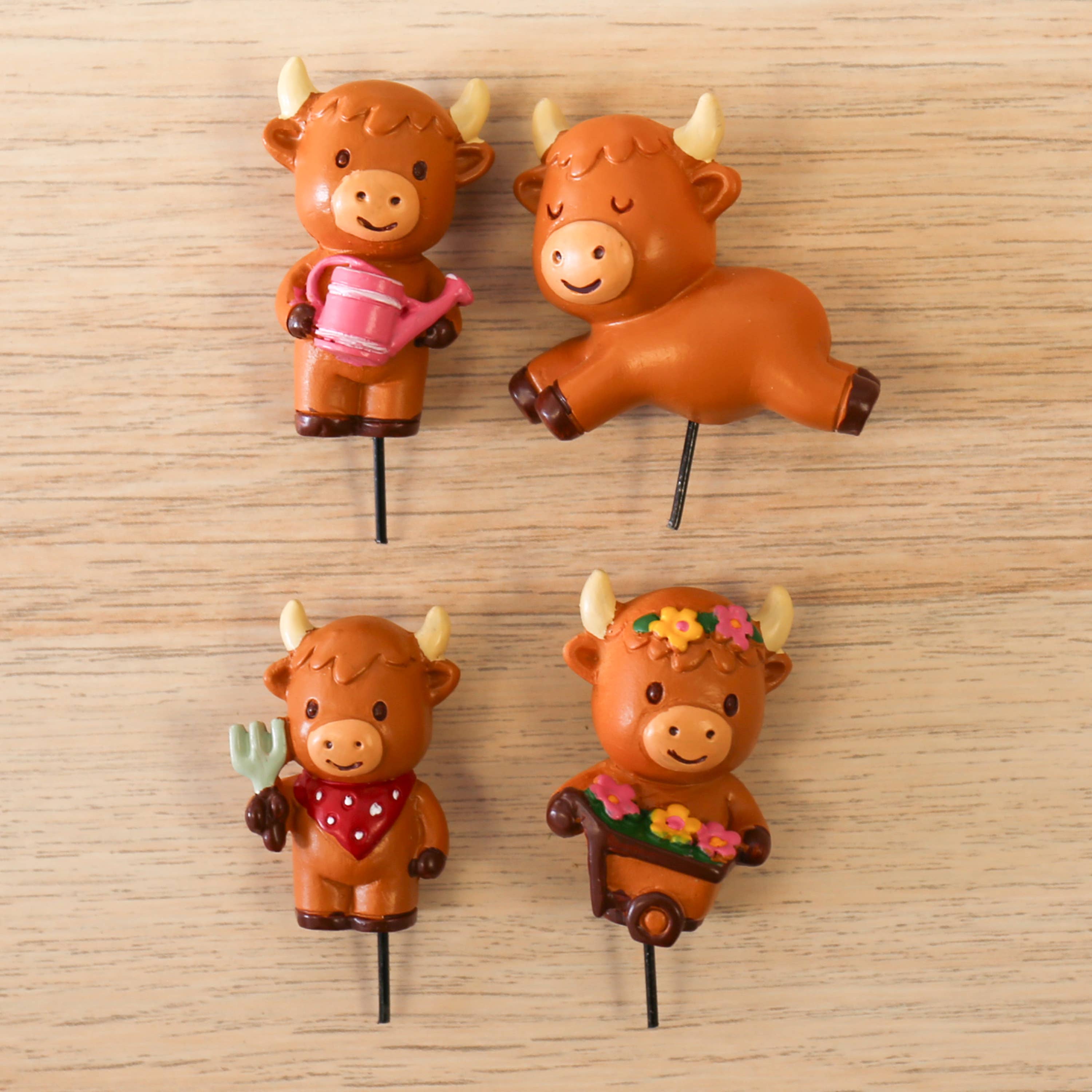Four Highland cow plant markers on metal stakes laid on pale wood