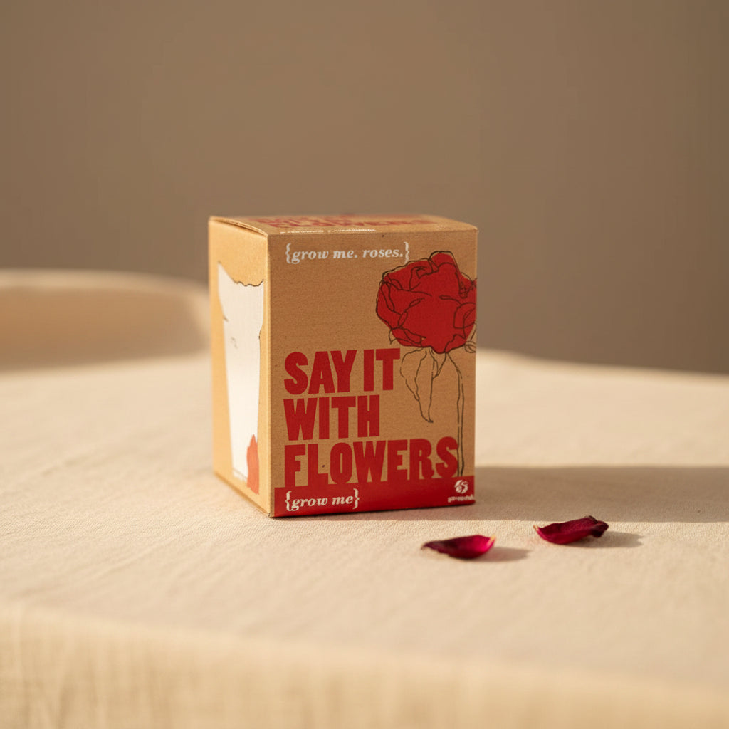 A small square cardboard box with a kraft-paper style front, featuring a red rose illustration and the text 'SAY IT WITH FLOWERS' and '{grow me, roses}' on a clean white background.