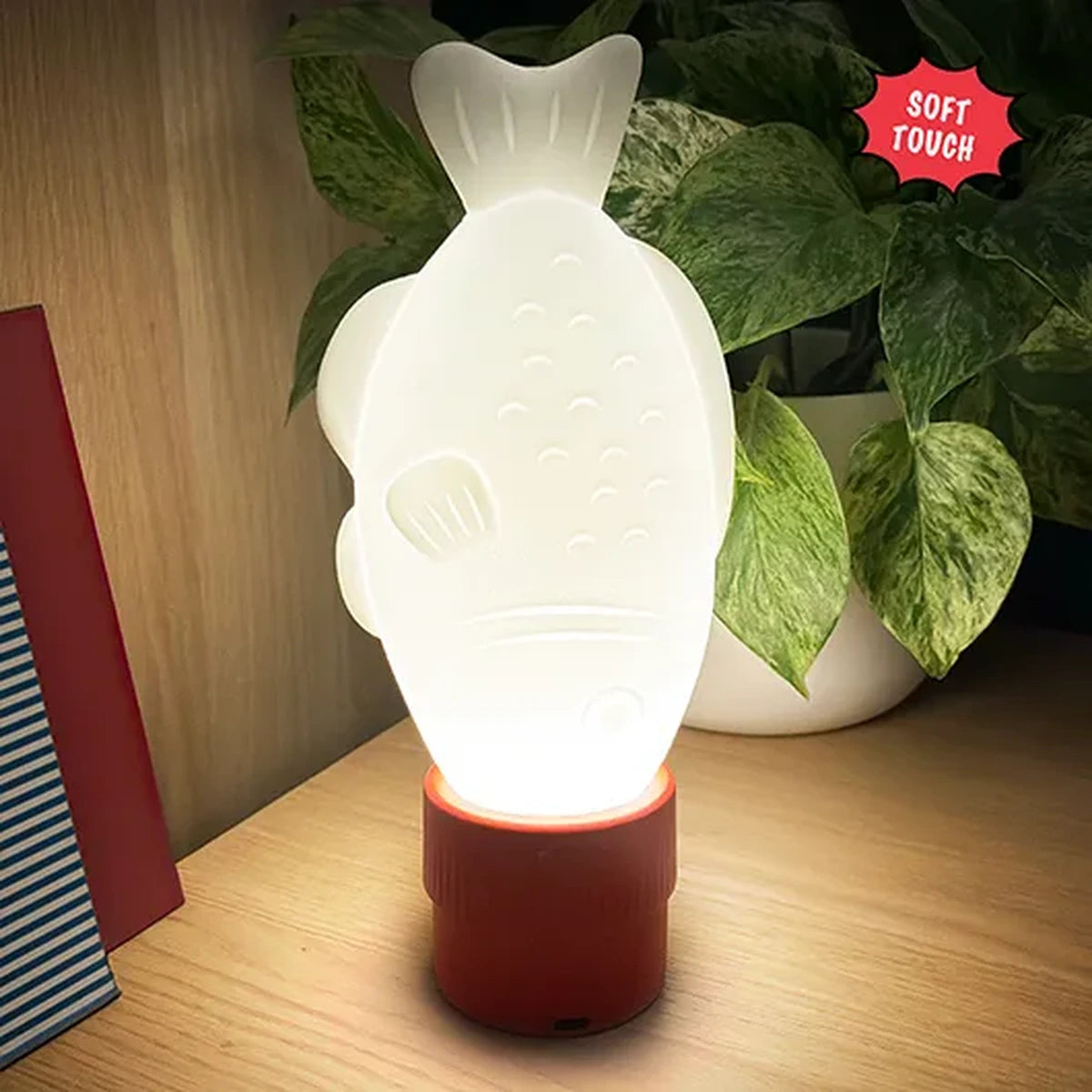 Soy sauce fish light glowing on a wooden shelf beside a plant
