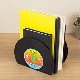 Record bookends holding books upright on a wooden desk beside plant