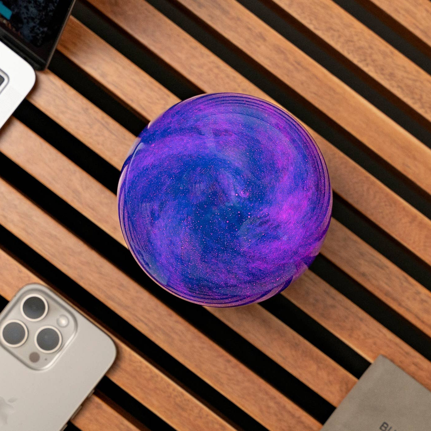 AstraGlass Galaxy Breeze orb from above glowing violet beside laptop