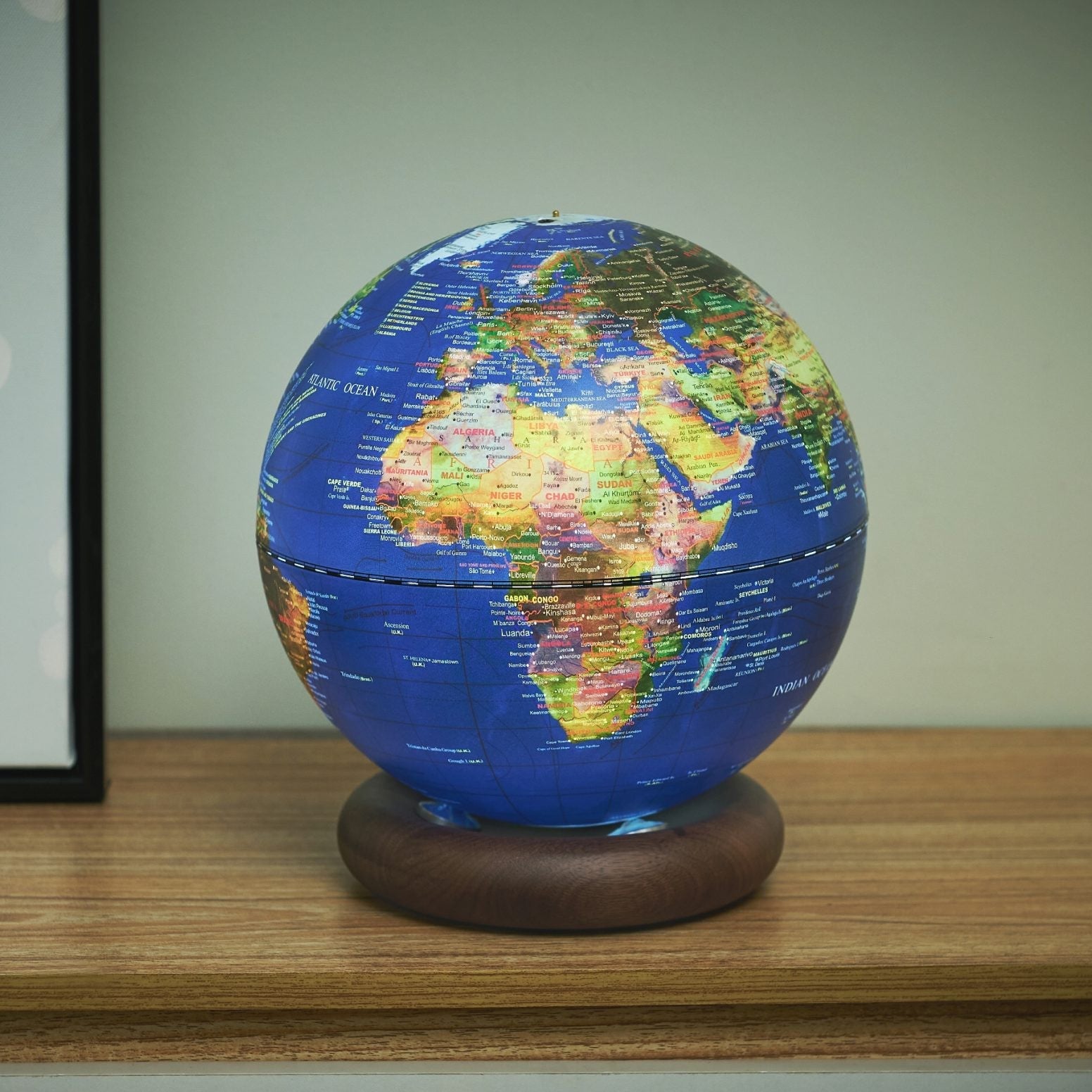 Dark blue globe light lit on a desk beside a picture frame and phone
