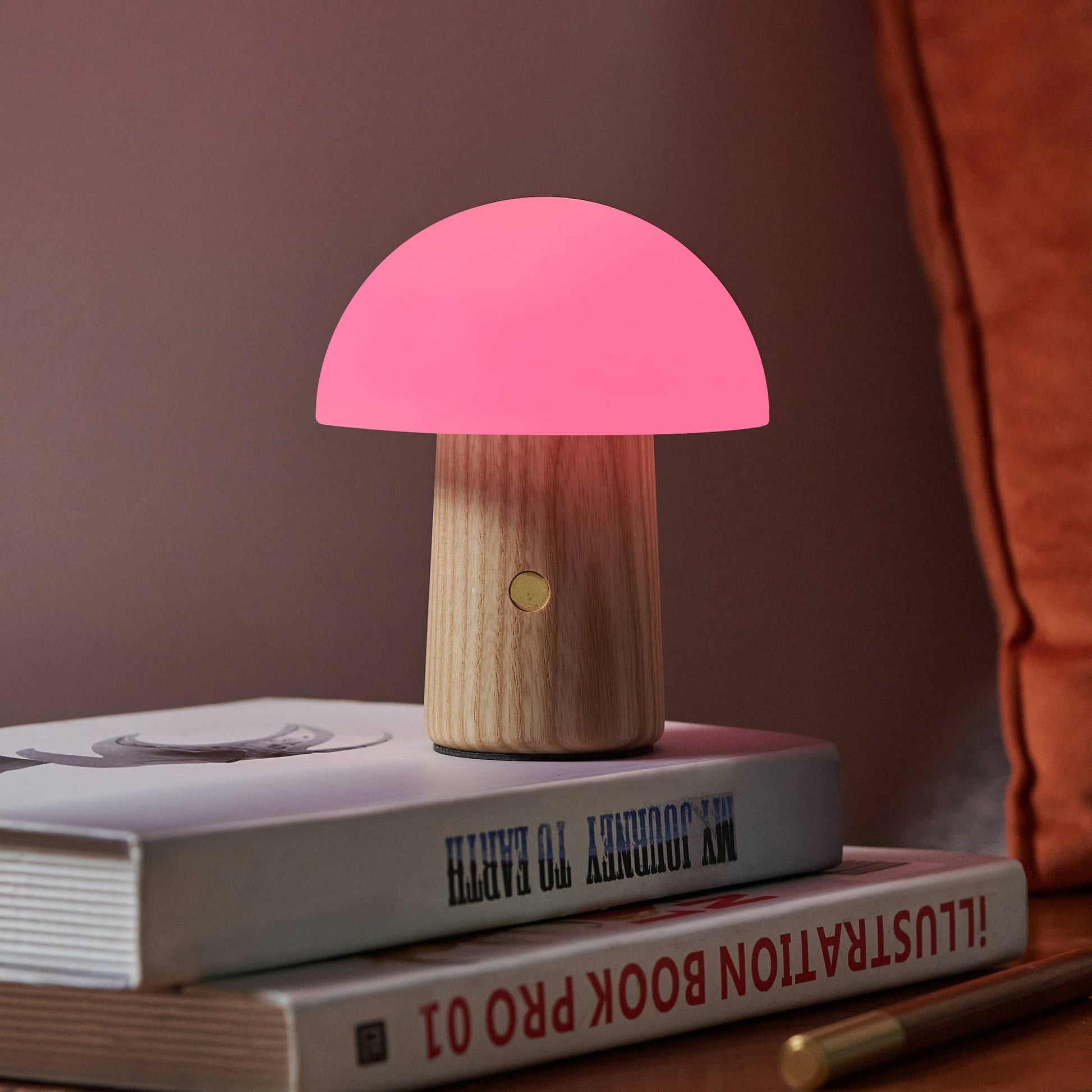 Mini Alice Mushroom Lamp in ash wood glowing pink on bedside books