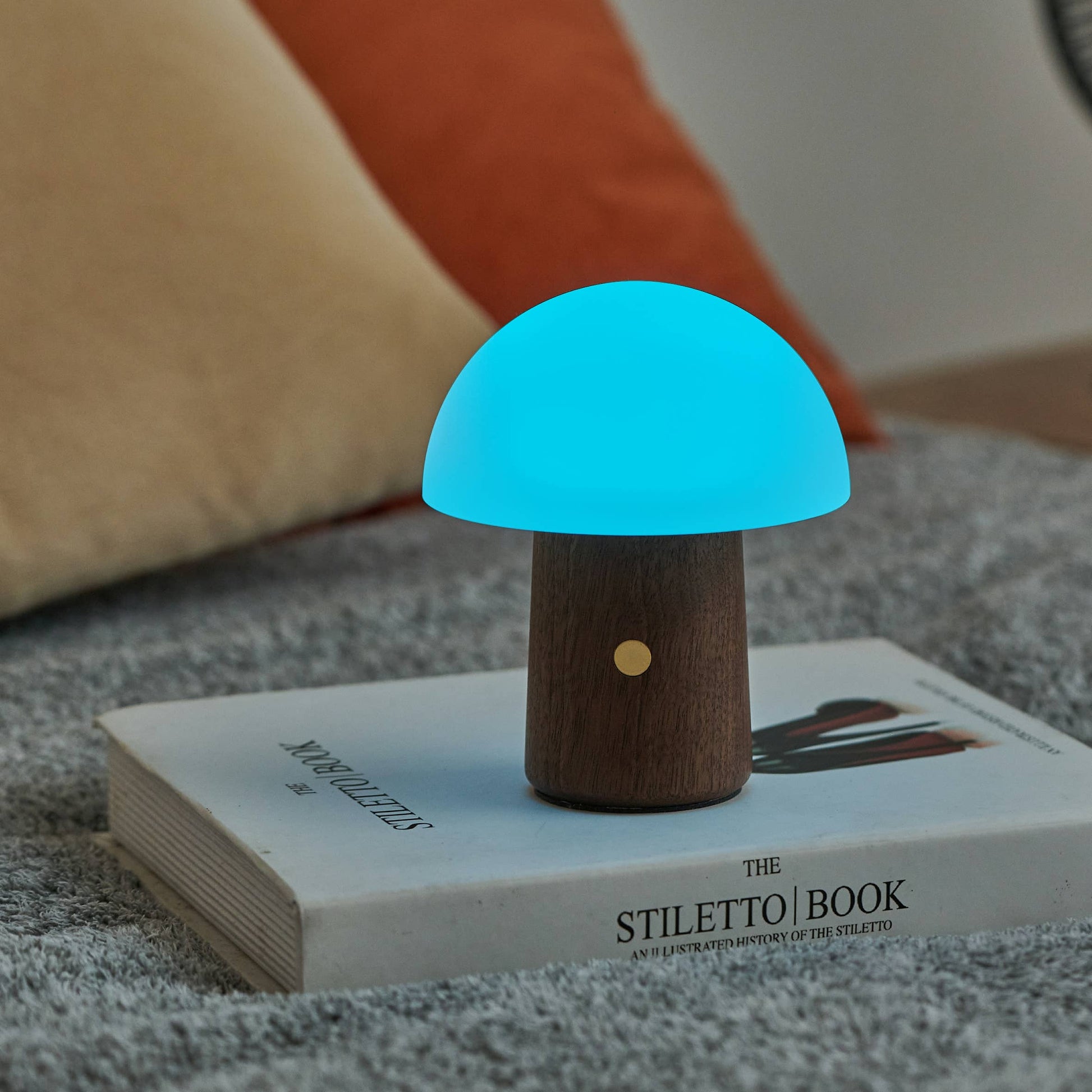 Walnut mushroom lamp glowing bright blue on a book on grey carpet