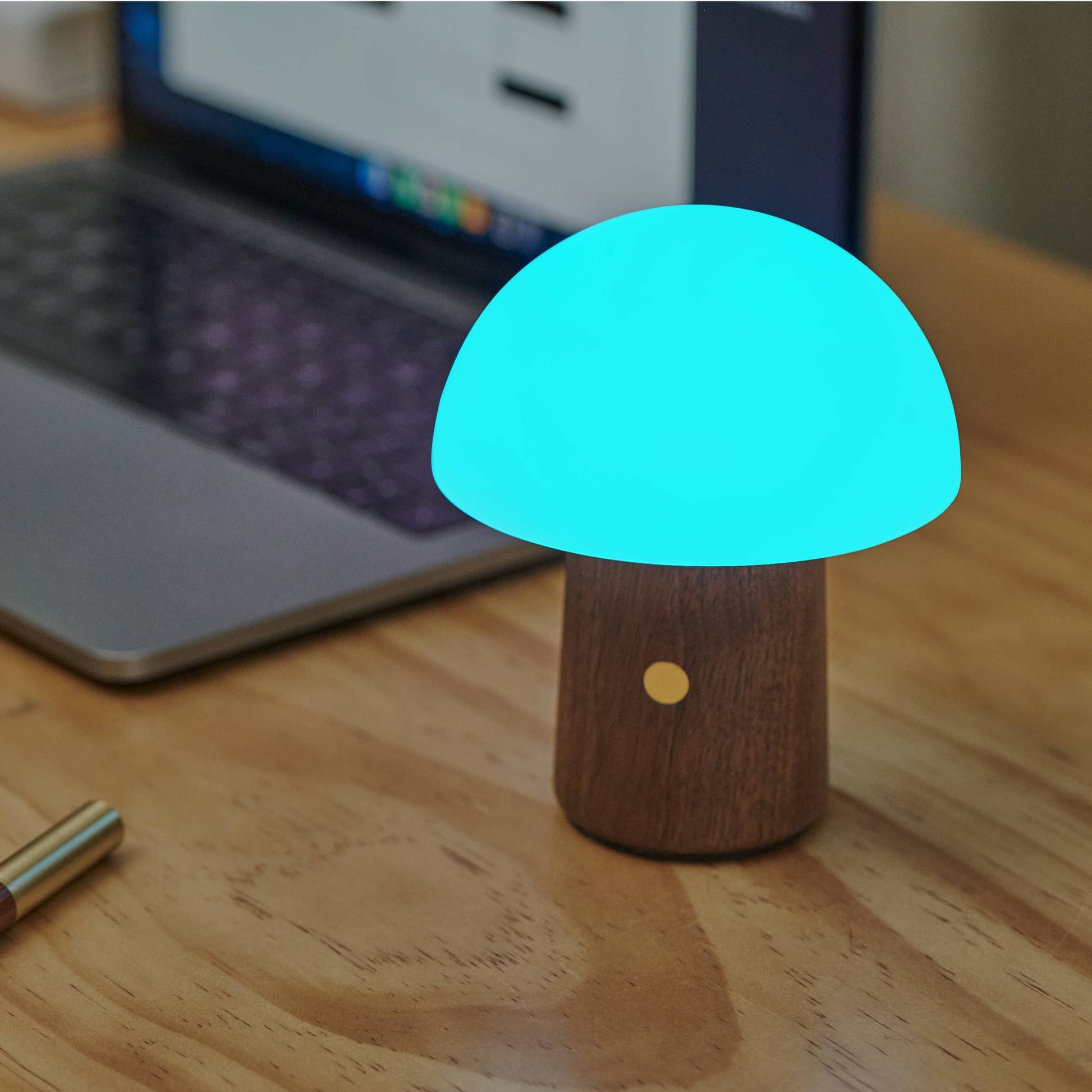 Walnut Alice Mushroom Lamp glowing blue on a desk beside a laptop