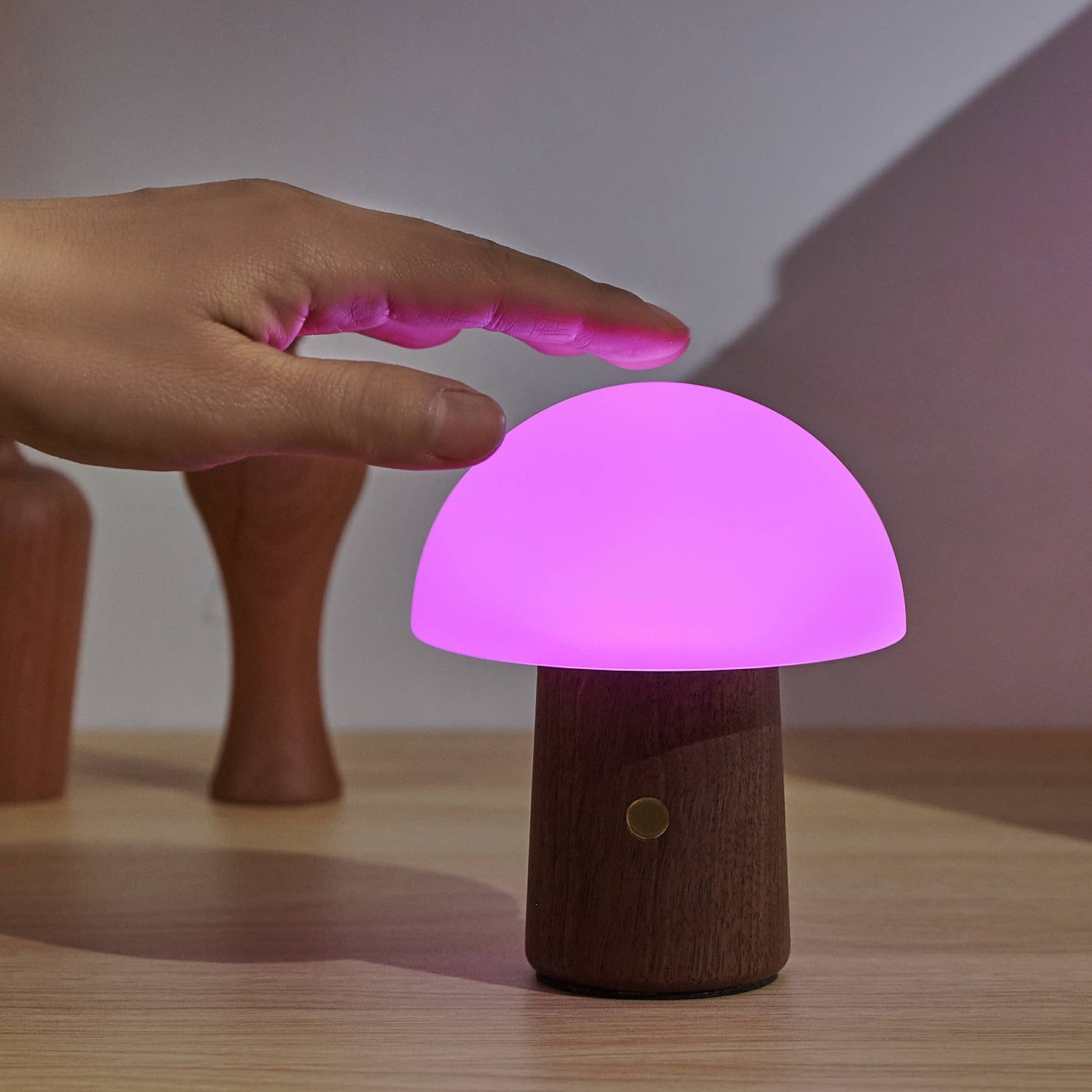 Alice Mushroom Lamp in walnut glowing purple as a hand taps the shade