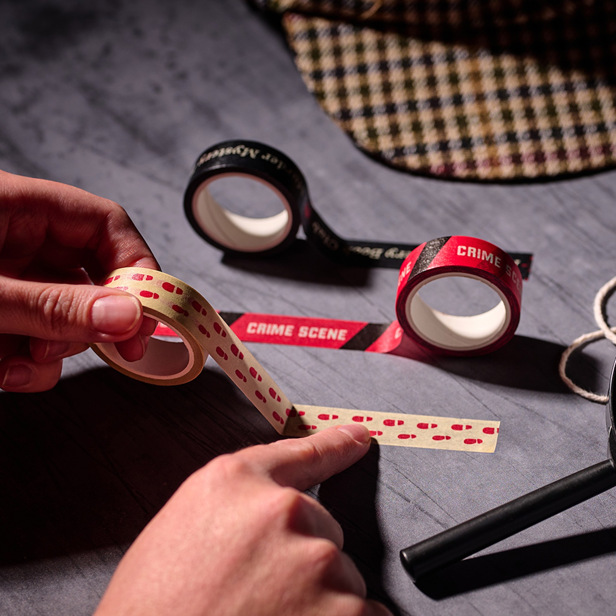 Hand tearing a strip of crime scene washi tape at a desk with scissors