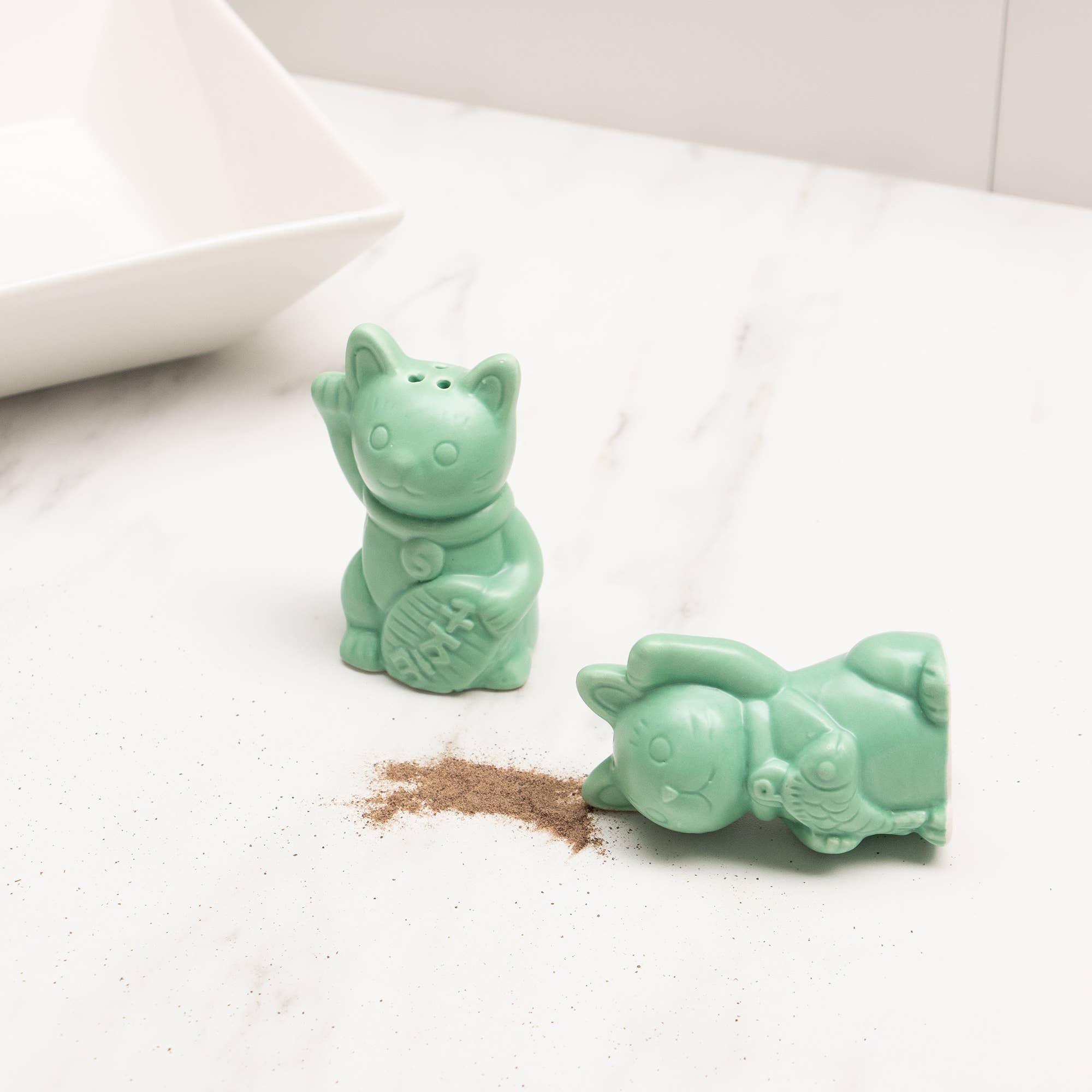 Green lucky cat salt and pepper shakers styled on a marble surface