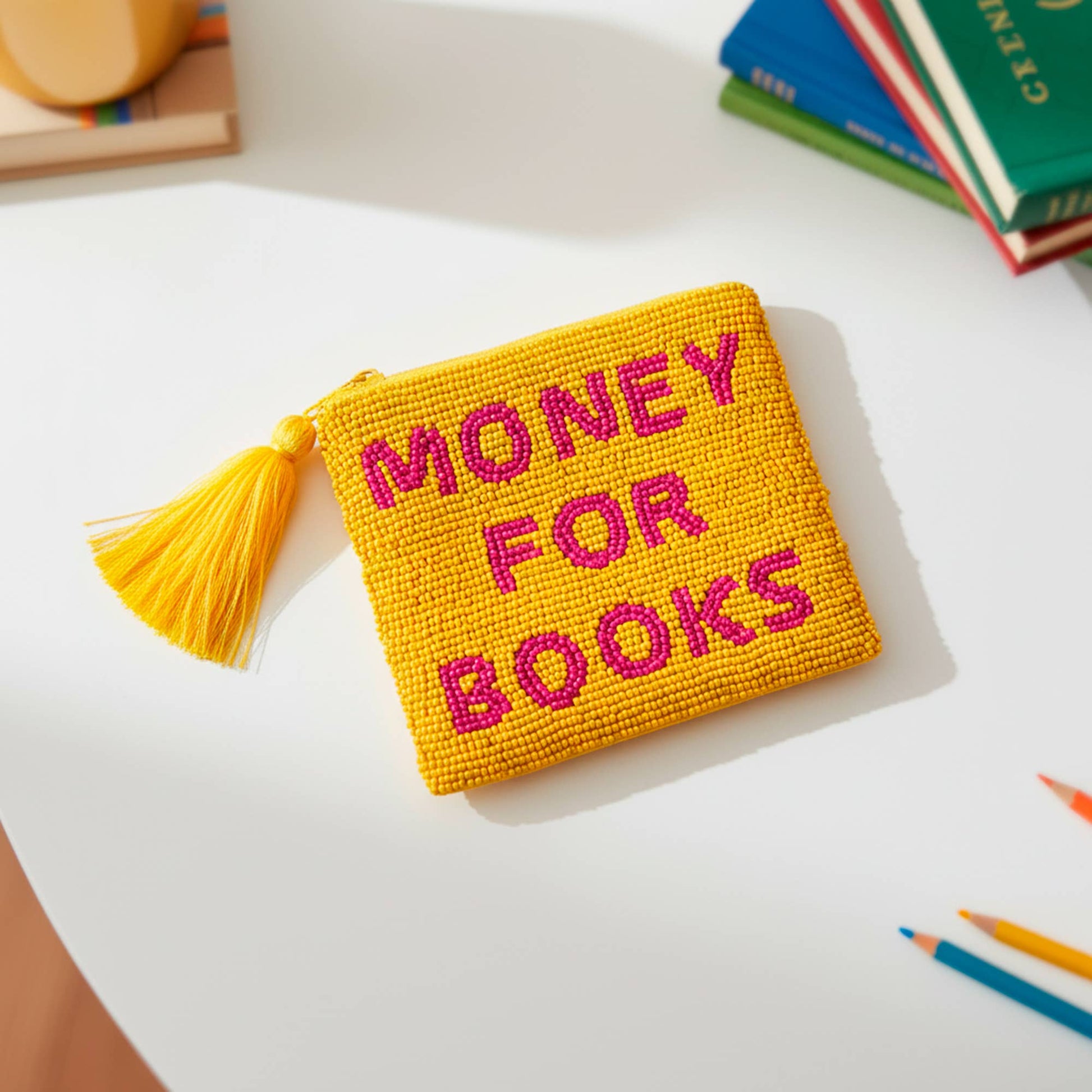 Yellow beaded Money For Books pouch with tassel, styled with books and pencils