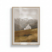 A framed art print depicting a small white church on a golden-brown hillside with snow-capped mountains in the background, set against a clean white wall.