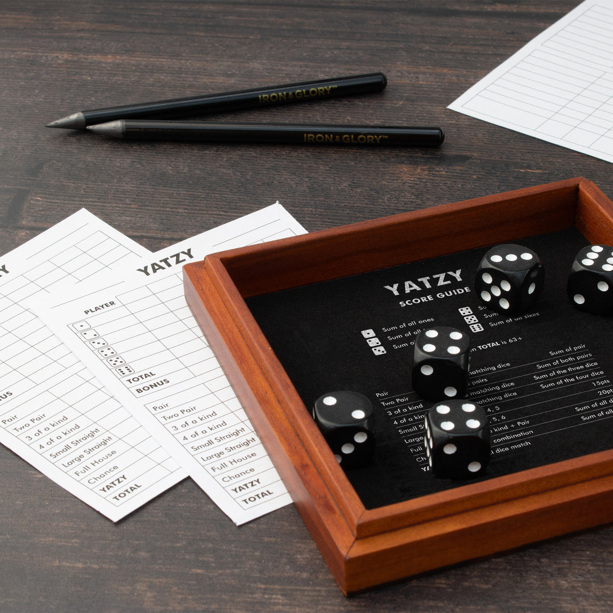 Iron & Glory Yatzy tray with dice, score sheets and pencils on a dark table