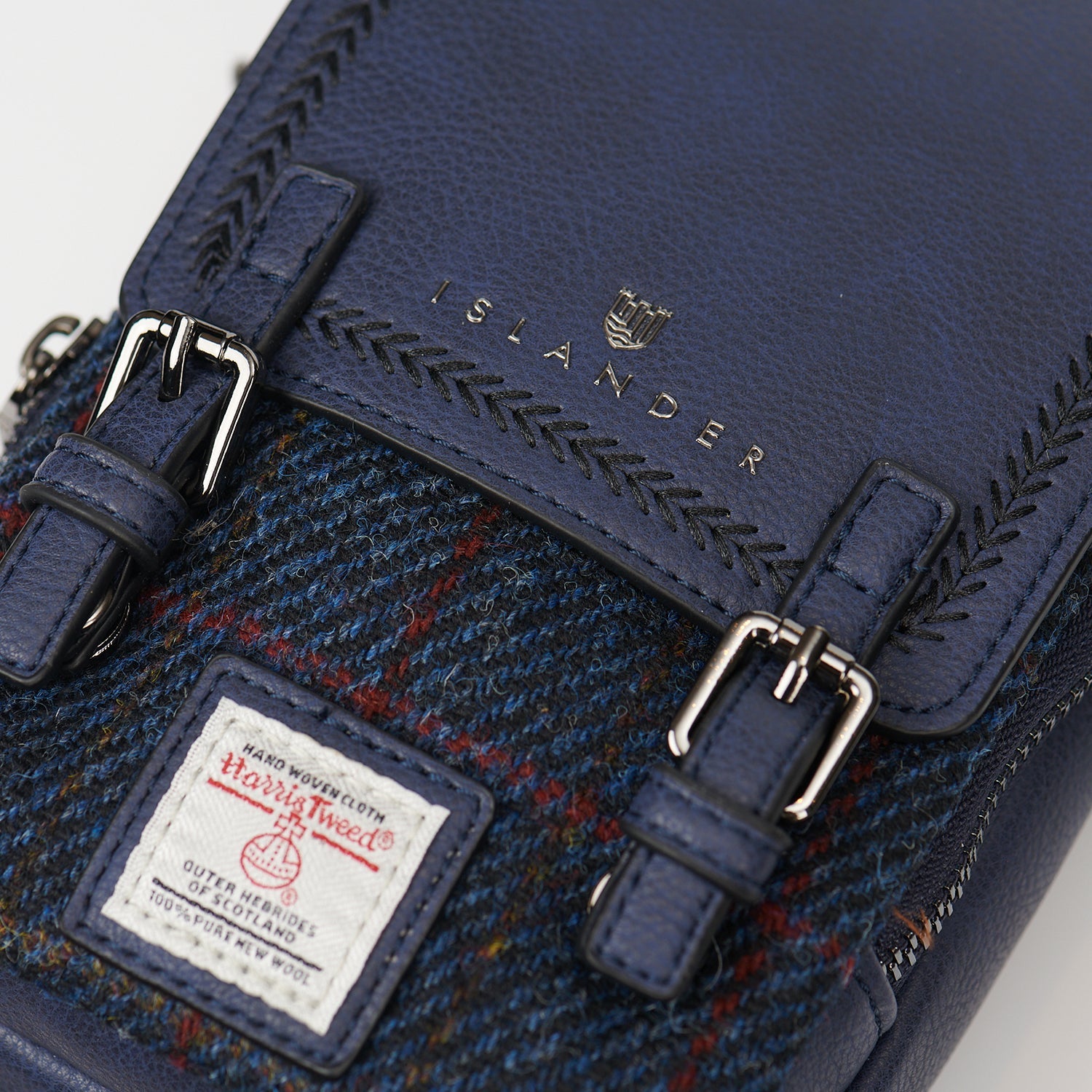 Navy crossbody bag detail showing embossed Islander logo and Harris Tweed label