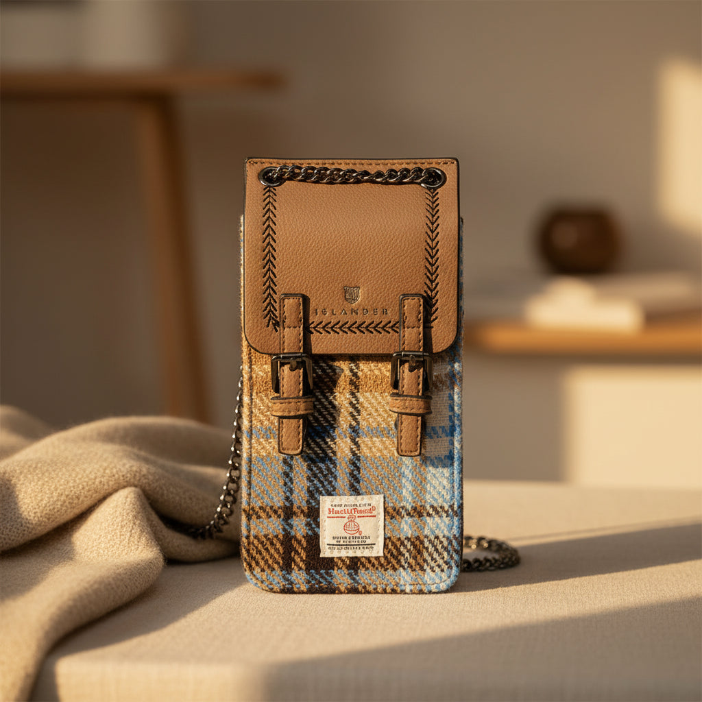 A Harris Tweed handbag with a brown leather top flap and chain strap, featuring a blue, brown, and beige plaid patterned body, a silver-tone buckle closure, and a Harriss Tweed label at the bottom.