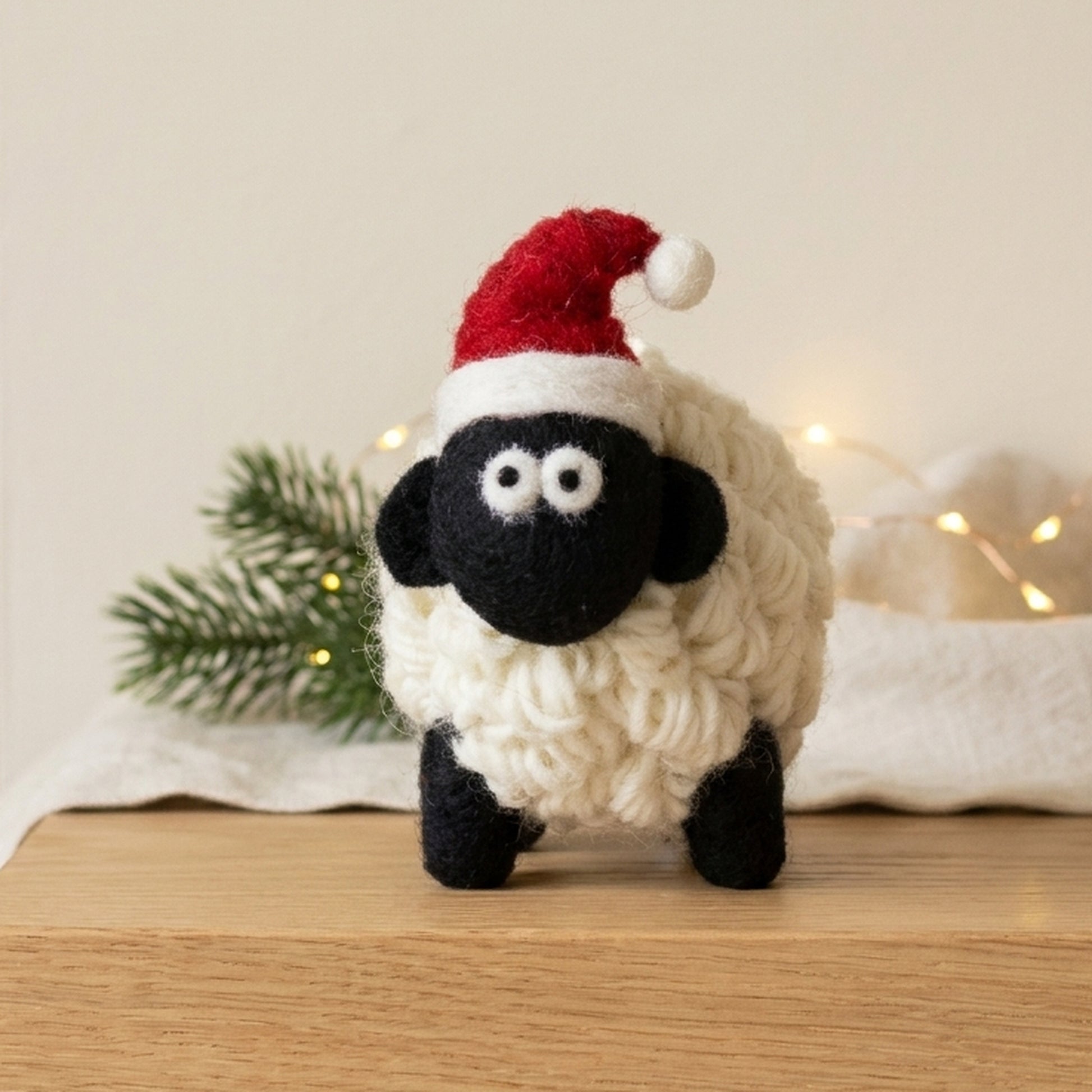 Wool Santa sheep on a wooden mantelpiece with pine and warm fairy lights