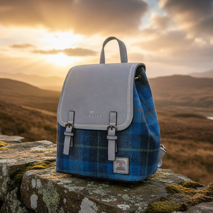 Harris Tweed blue tartan backpack on stone wall with Scottish highland sunset