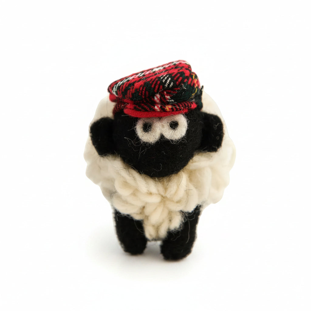 Knitted wool sheep keyring in a red tartan flatcap, on a plain white background.