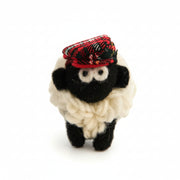 Knitted wool sheep keyring in a red tartan flatcap, on a plain white background.