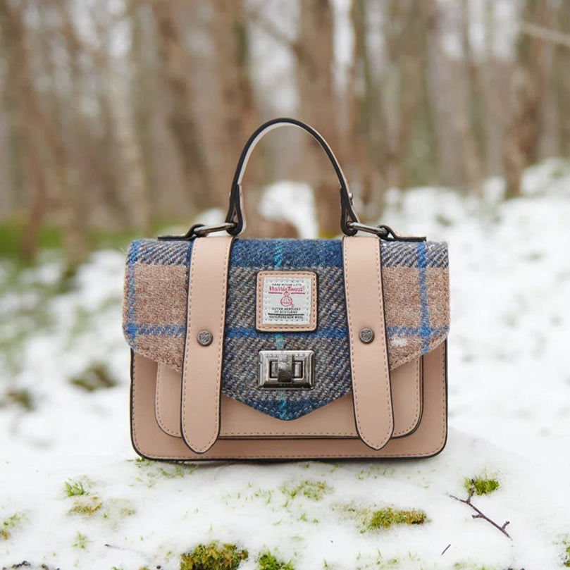 Lifestyle shot of navy & beige satchel on snow-covered moss in woodland.