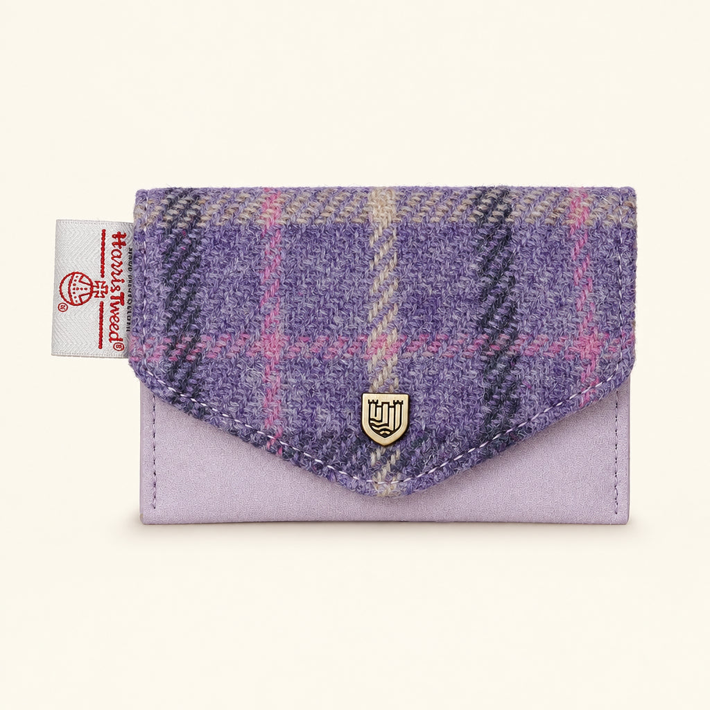 A small envelope-style wallet in lavender suede with a purple and pink plaid wool flap. A small gold shield logo is centered on the flap, and a fabric brand tag is visible on the left edge.