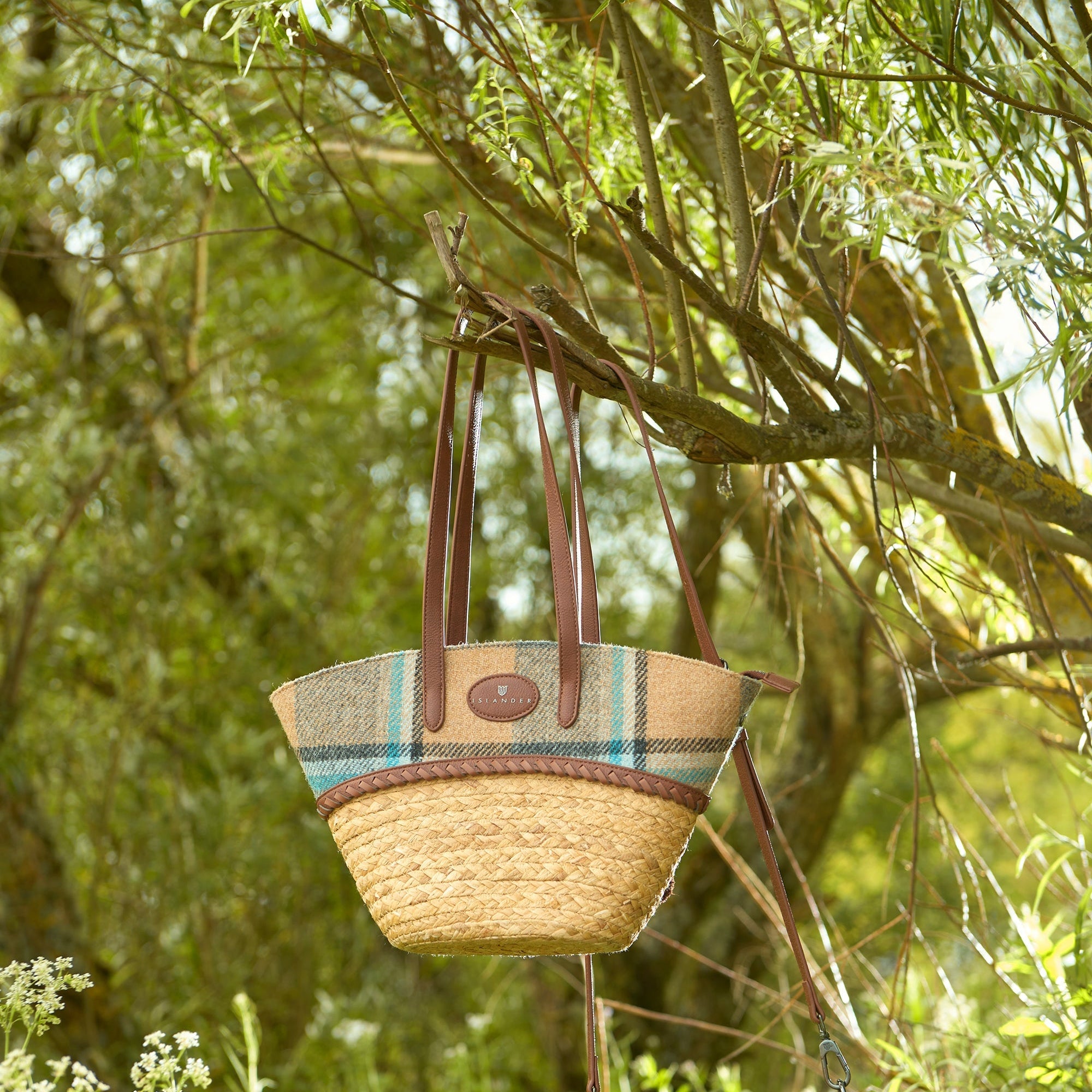 Islander check basket bag hanging from a tree branch by its strap