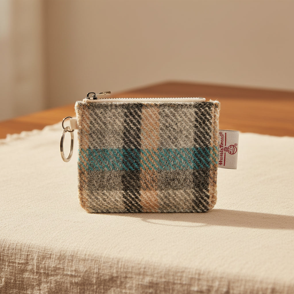 A small zippered coin pouch with a plaid pattern in beige, gray, black, and turquoise blue, featuring a silver metal key ring and a white brand tag that reads 'Harris Tweed'.